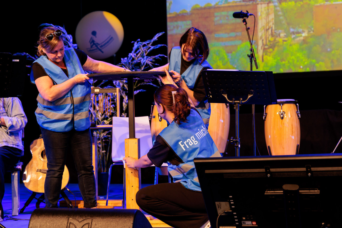 KAD team members demonstrate the height adjustment of a table on stage during the Lebenshilfe NRW Cultural Festival.