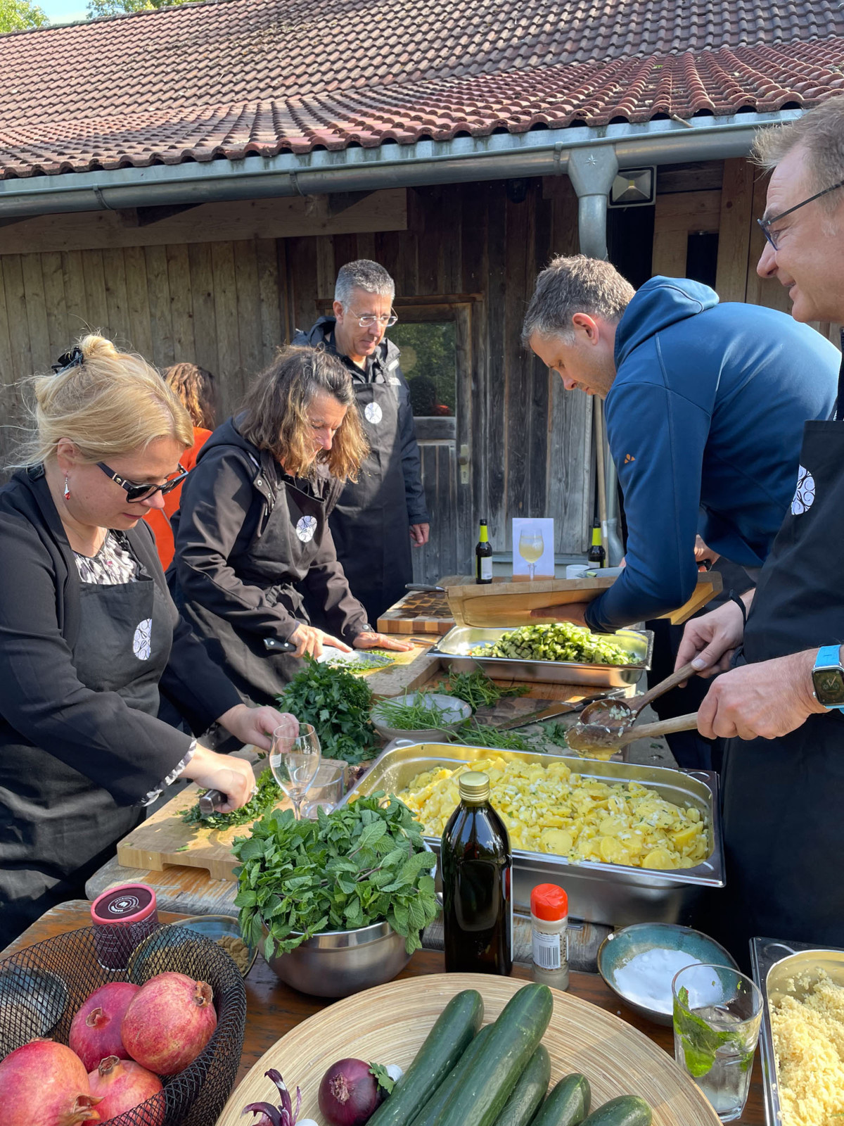Teilnehmende bereiten bei einem Teambuilding-Event gemeinsam ein BBQ zu und schneiden frische Zutaten an einer Arbeitsstation im Freien.