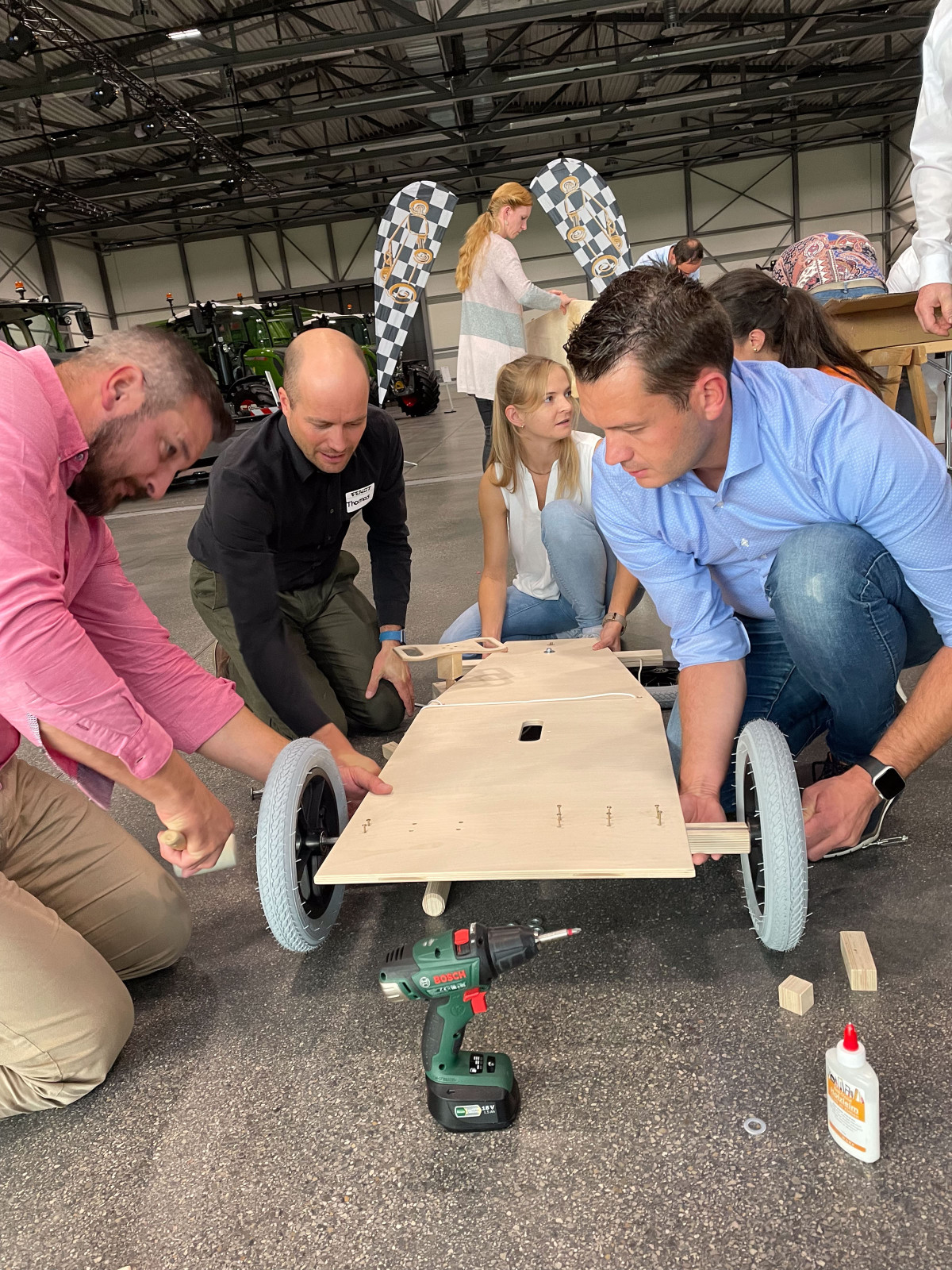 Teilnehmende bauen bei einem Fendt Teambuilding-Event gemeinsam eine Seifenkiste und montieren das Fahrgestell an eine Holzplatte.