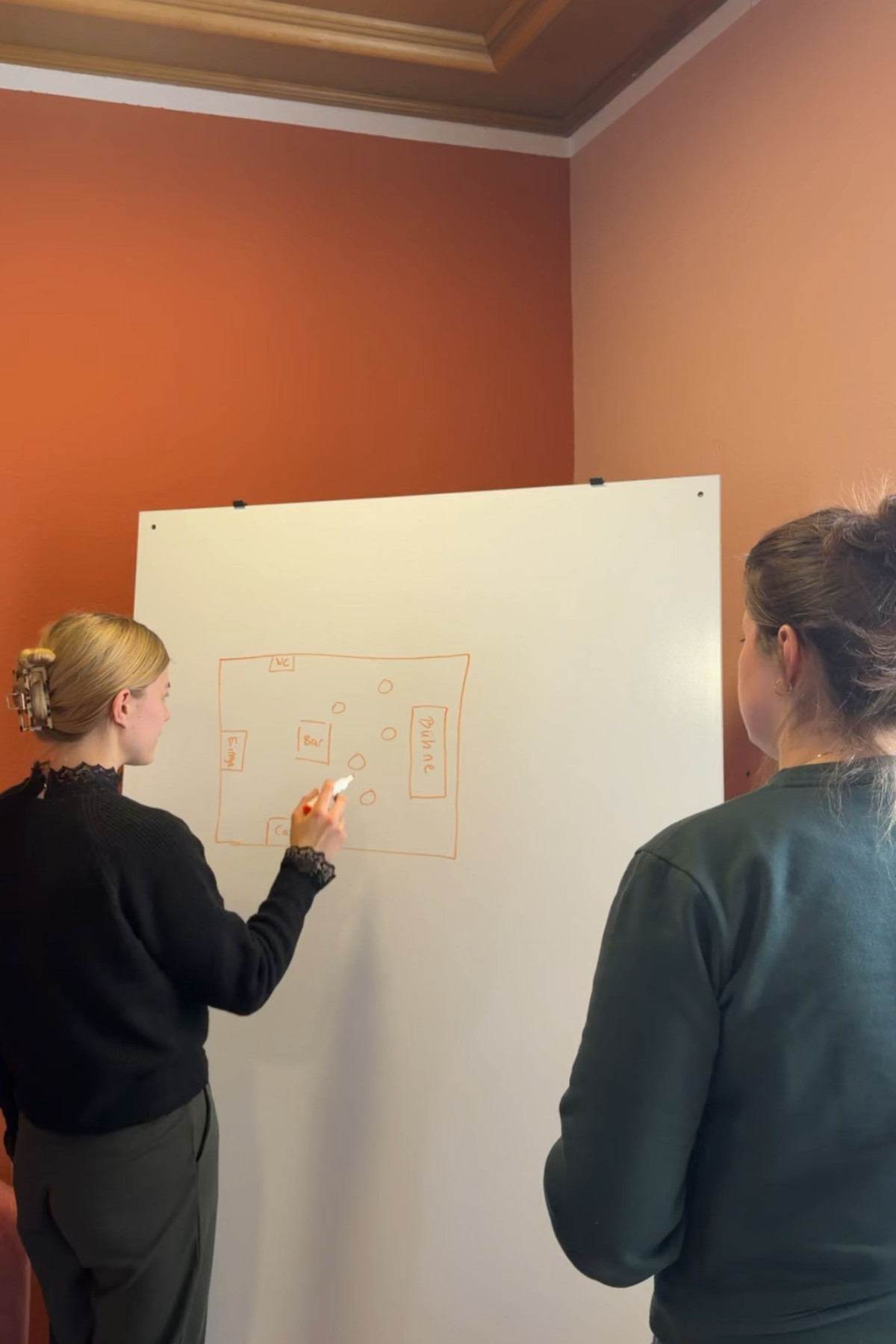 Dual student Veronika explains a sketch on a whiteboard to a colleague during a meeting at the KAD office.