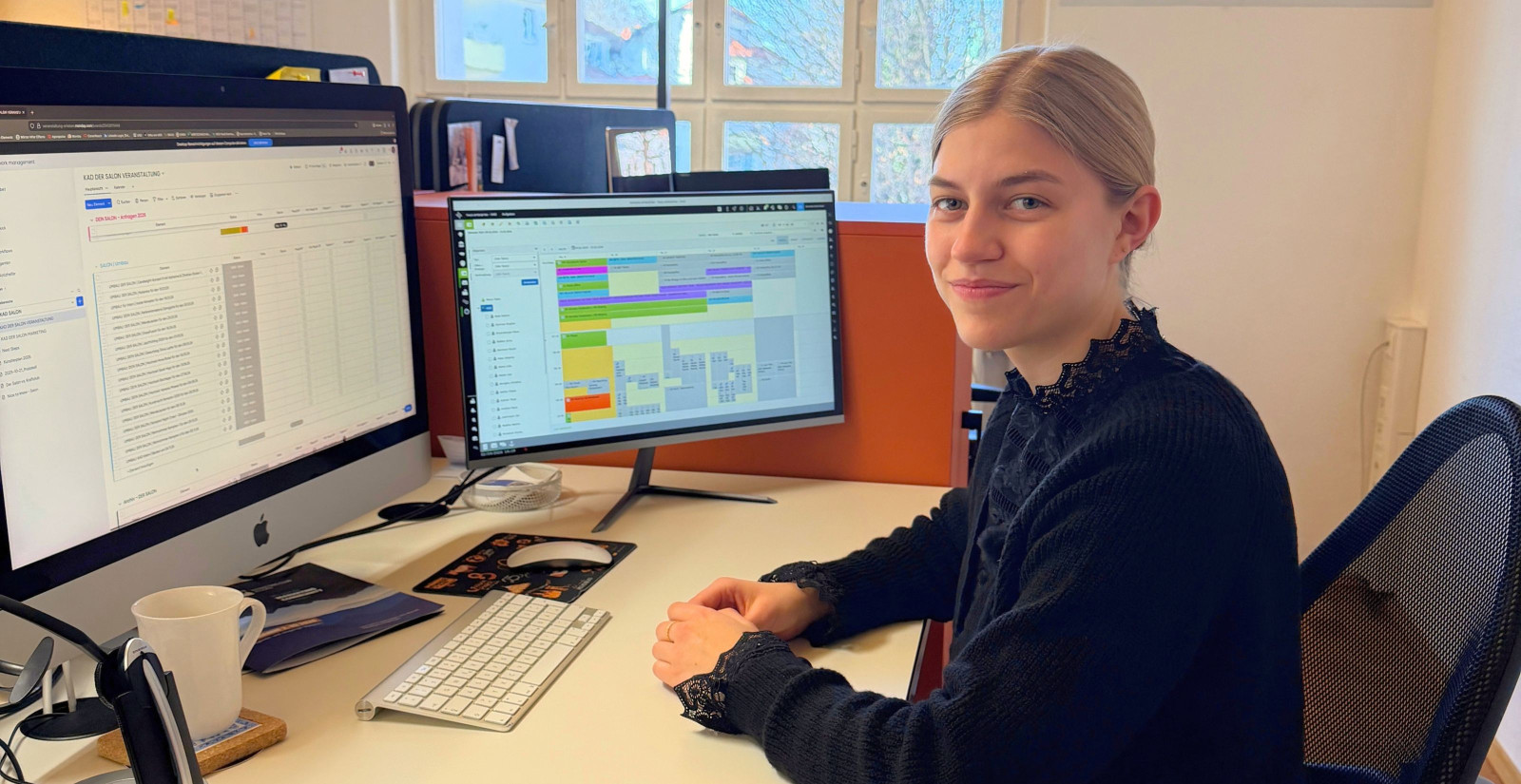 Dual student Veronika sits at her desk at KAD in front of two monitors displaying event planning software.