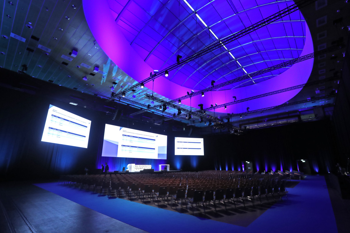 Seated congress hall with stage, presentation screens, and lighting design before the event begins.