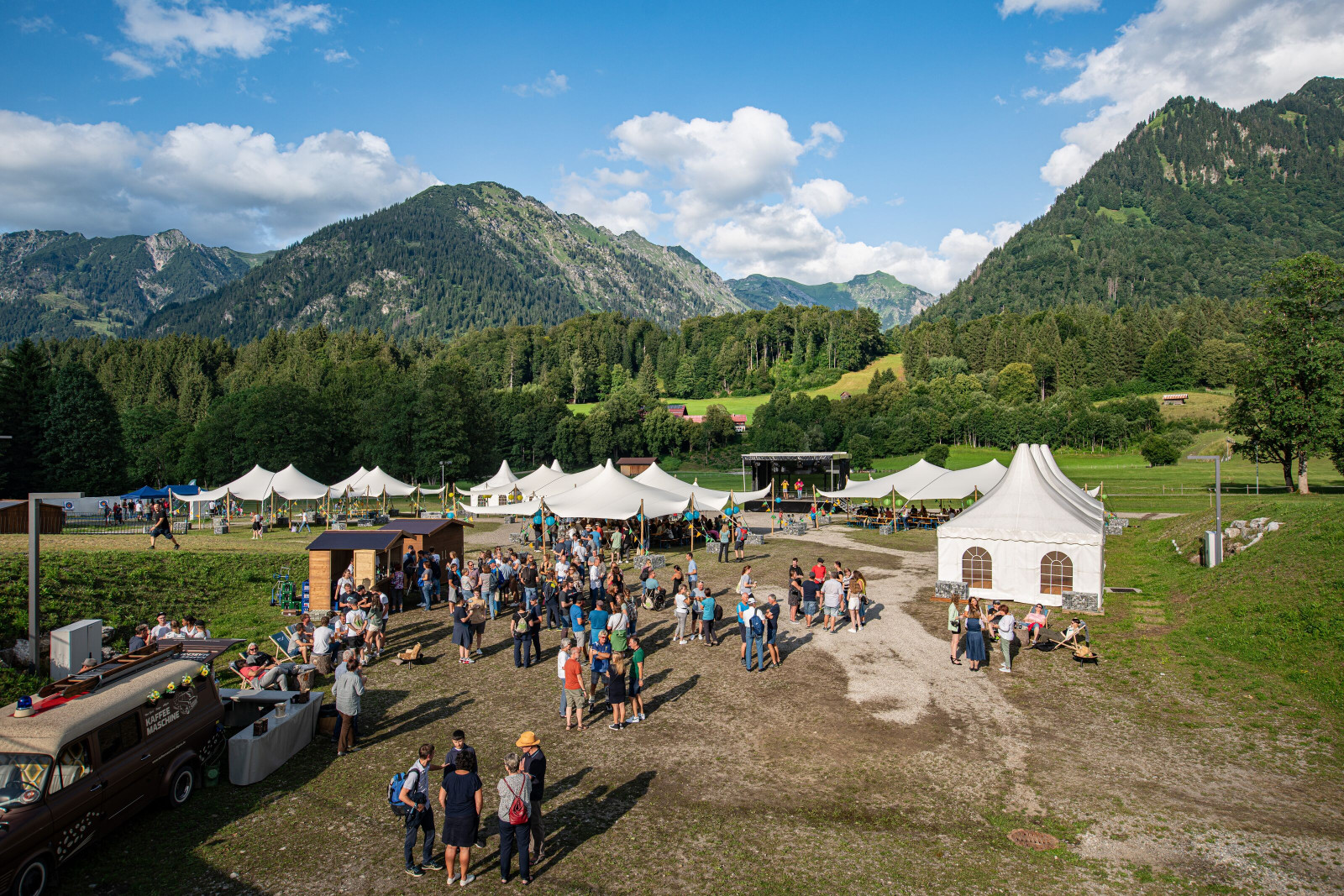 Luftaufnahme des OTT-JAKOB Firmenjubiläums im Nordic Zentrum Oberstdorf mit Stretchzelten, Bühne und Gästen vor der Bergkulisse der Allgäuer Alpen.