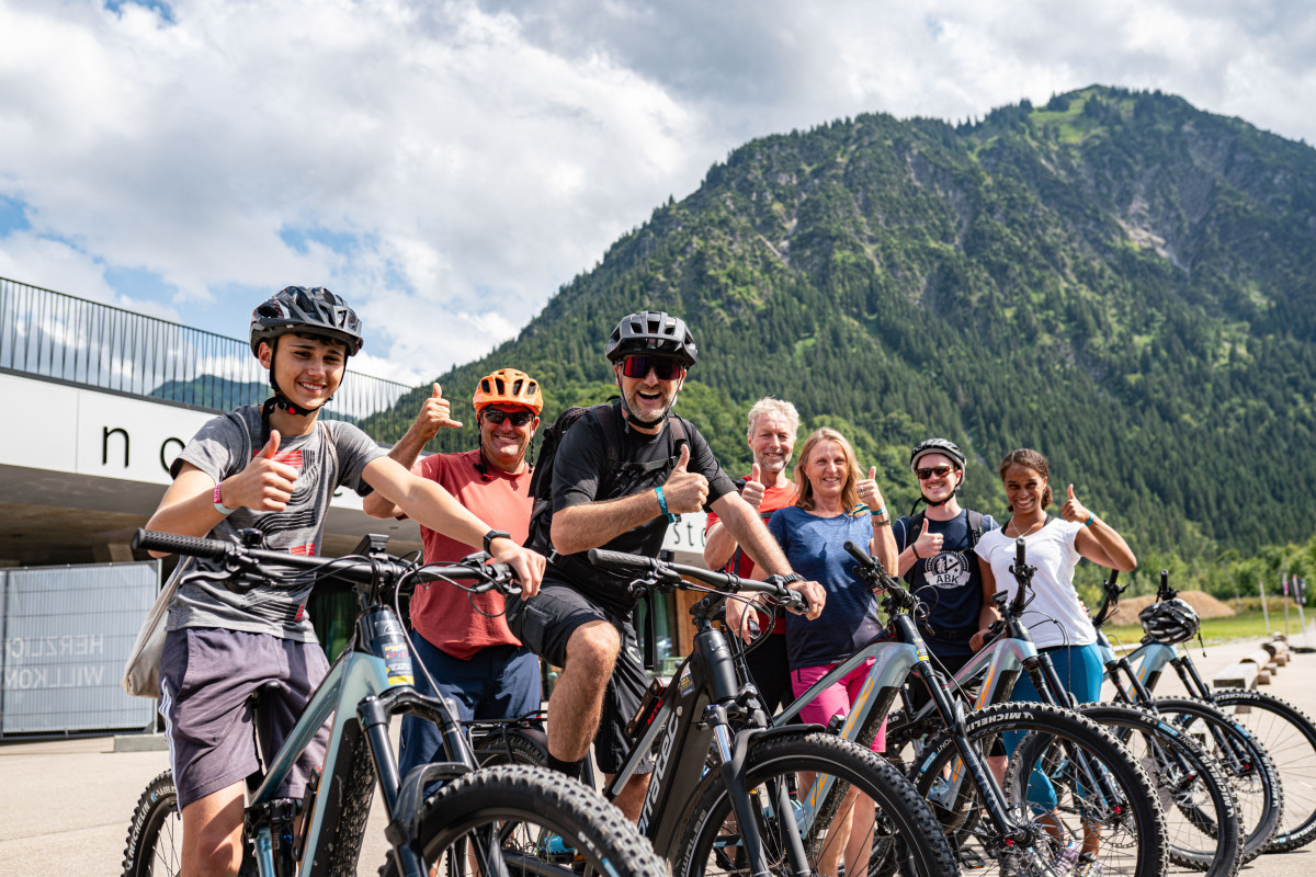 Mitarbeitende und Familienangehörige von OTT-JAKOB posieren mit Mountainbikes vor der Bergkulisse der Allgäuer Alpen.
