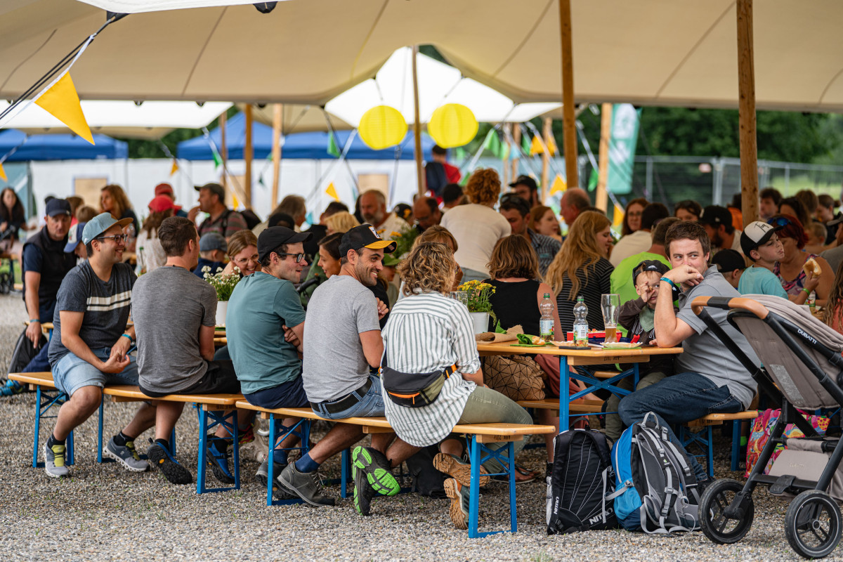 Mitarbeitende und Familienangehörige von OTT-JAKOB sitzen gemeinsam an langen Tischen unter einem Stretchzelt beim Firmenjubiläum in Oberstdorf.