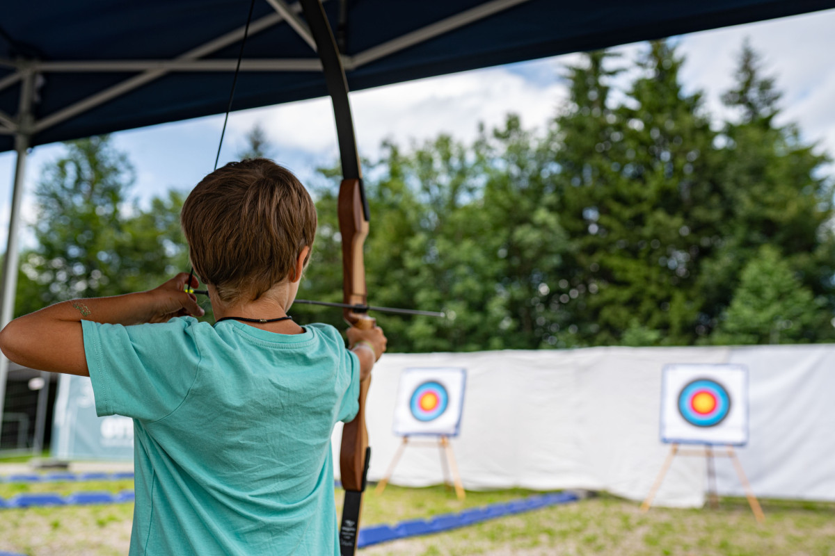 Kind nimmt beim OTT-JAKOB Firmenjubiläum an einem Bogenschieß-Workshop teil und zielt mit Pfeil und Bogen auf eine Zielscheibe im Freien.