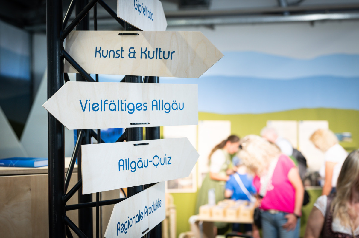 Signpost with themes like culture, diversity, and an Allgäu quiz for orientation at the booth.