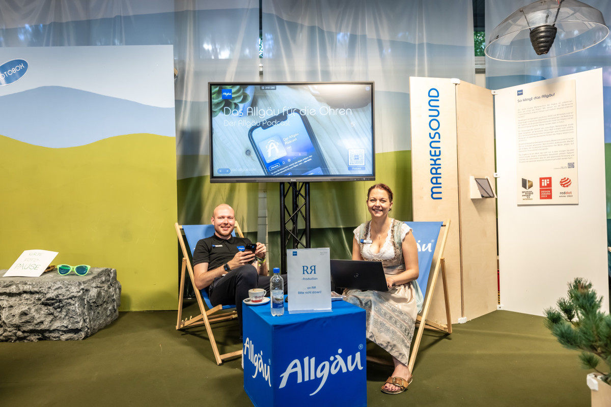 Two booth hosts sit relaxed at the info desk and chat with guests.