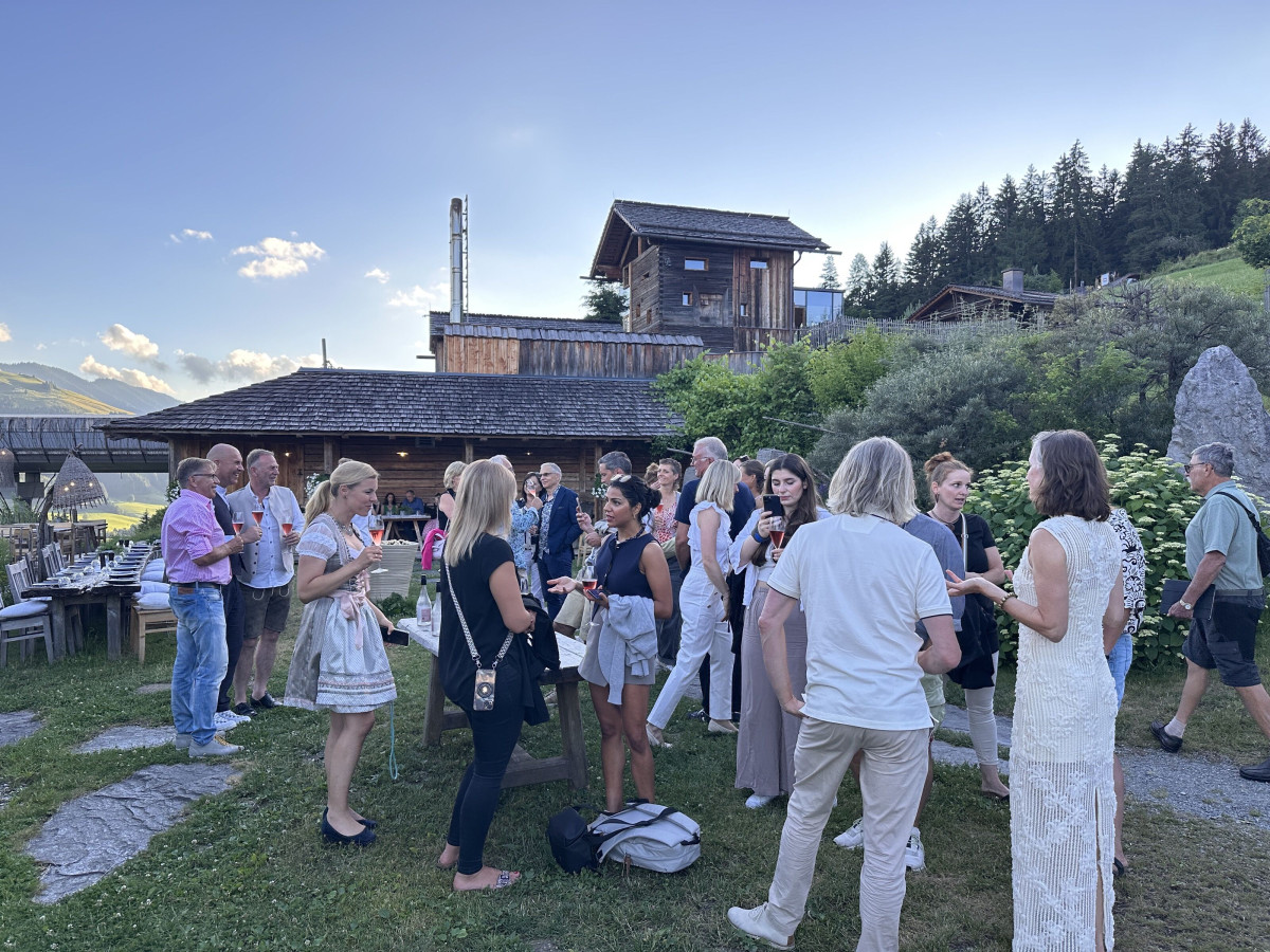 Guests in conversation at an outdoor event in front of a mountain hut.