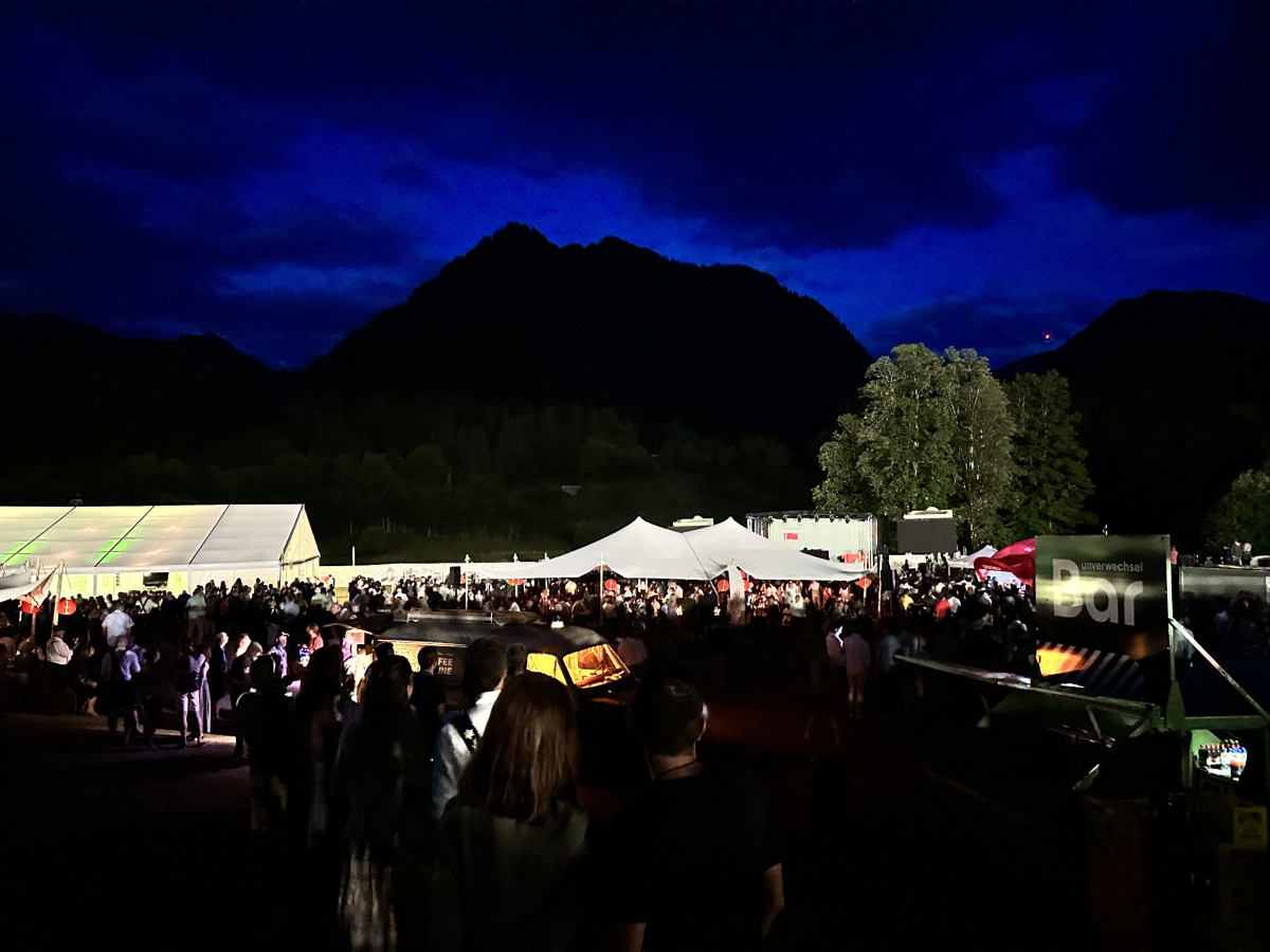 Festival grounds at night with illuminated tents and mountain silhouette.