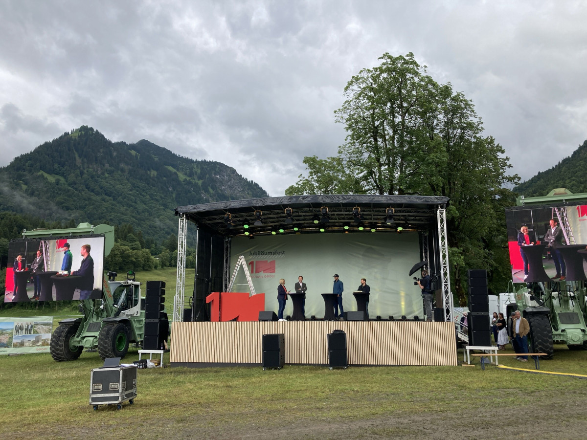 Outdoor stage with event technology in front of a mountain landscape.