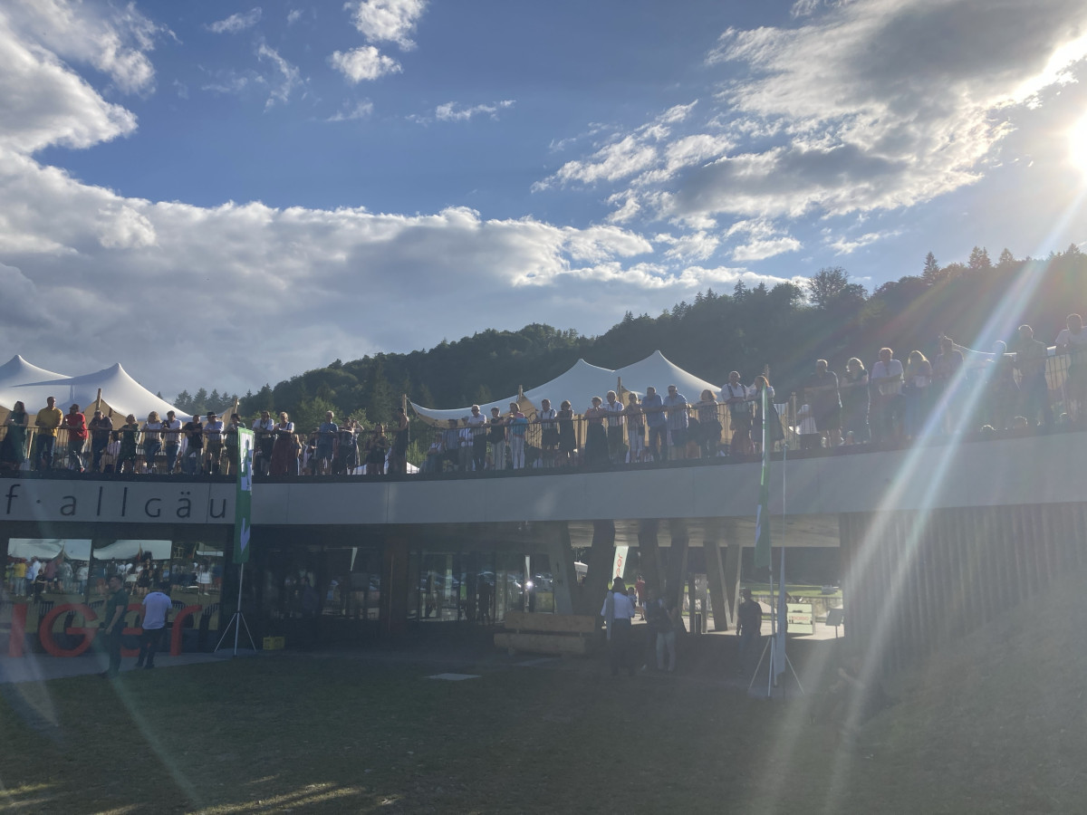 Visitors on the anniversary grounds in front of a mountain panorama.