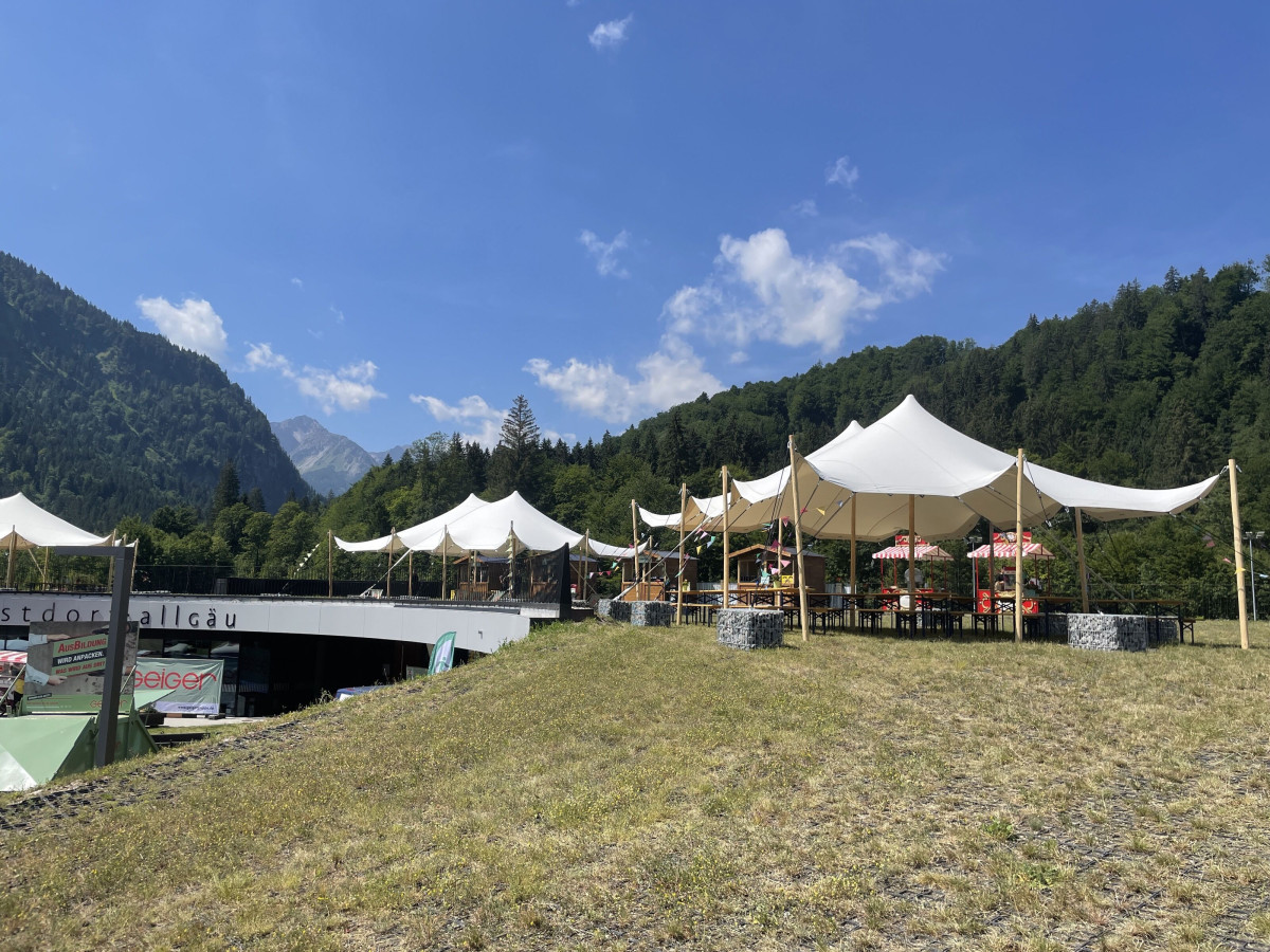Event tents on a meadow against an alpine mountain backdrop.