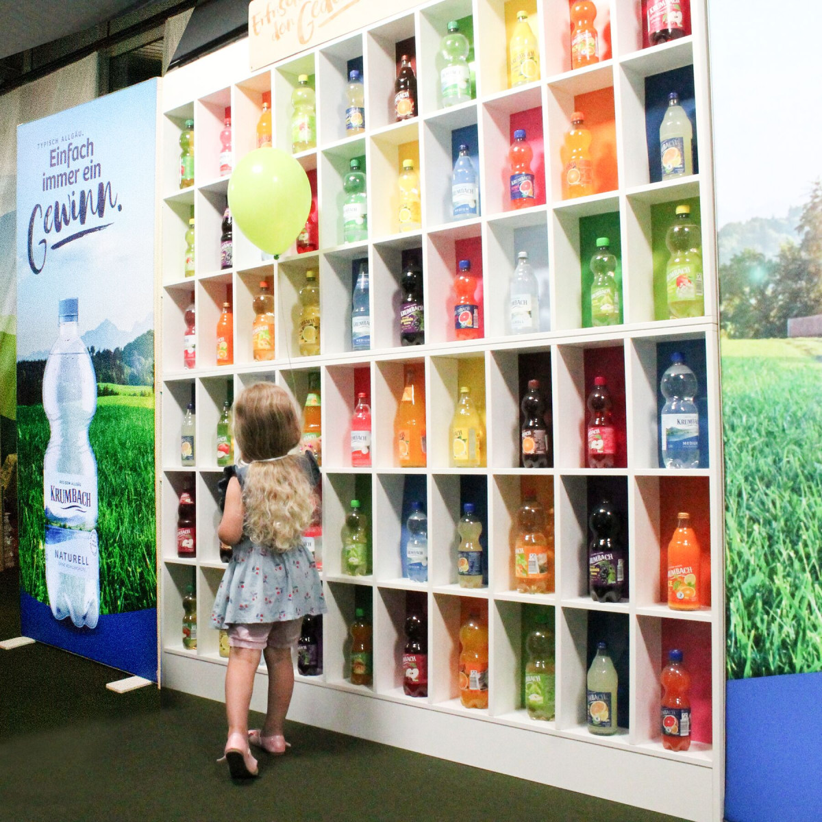 A child stands in front of a colorful beverage wall and explores the memory game at the booth.