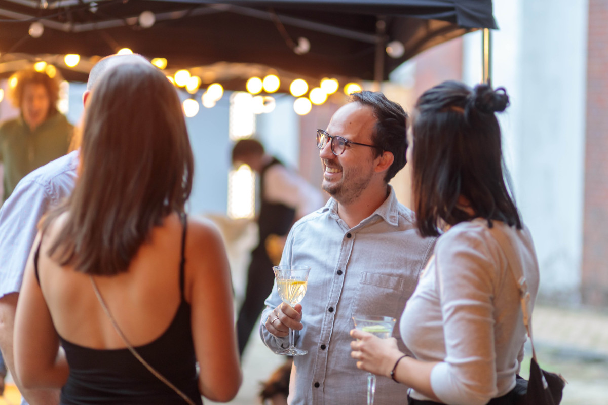 Event guests in lively conversation while holding glasses of sparkling wine.