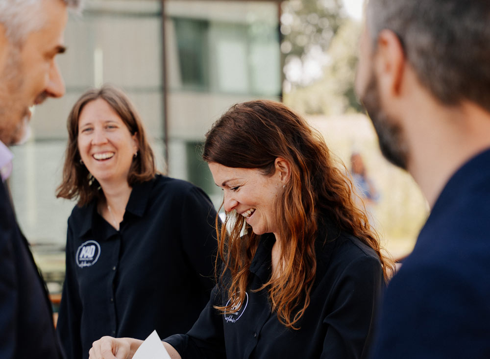 Foto von zwei lachenden Eventmanagerinnen der Eventagentur KAD aus Kempten und Herten, welche zwei glückliche Gäste für eine Veranstaltung registrieren im Rahmen des Teilnehmermanagements.